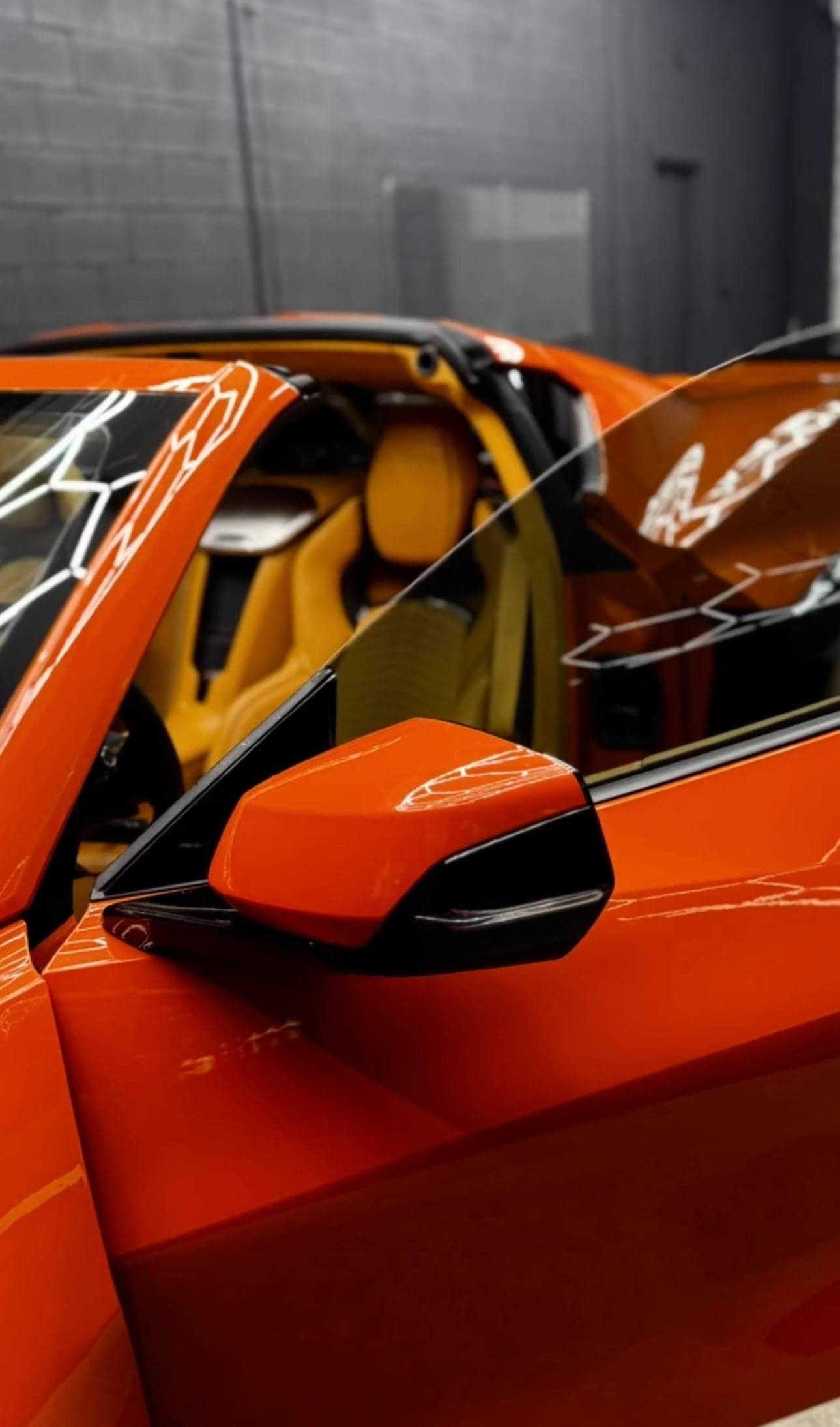 Orange Chevrolet Corvette with the door open, showing its tinted side glass and tan interior